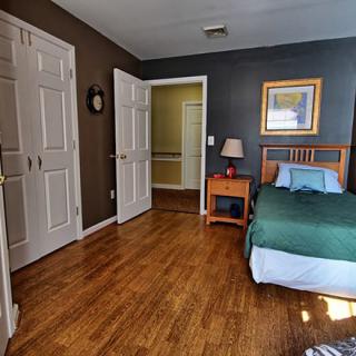 A cozy bedroom with wooden floors, a bed, nightstand with a lamp, and a closet.