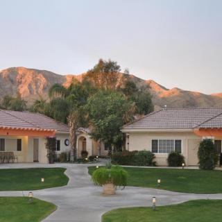 A peaceful residential area with houses, palm trees, and mountains at sunset.