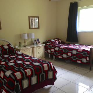 A cozy bedroom featuring two twin beds with patterned bedspreads, a shared nightstand with lamps, and a window providing natural light.