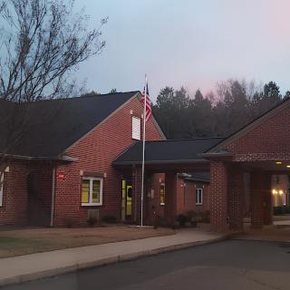 A brick building with a flagpole displaying the American flag at dusk.