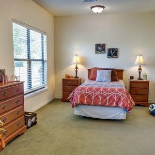 A cozy bedroom with a bed, nightstands, and dressers, featuring warm lighting.