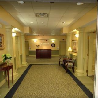 A well-lit lobby area featuring a reception desk, carpeted floor, and decorative elements such as paintings and lamps.