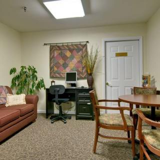 A small office with a sofa, desk, and chairs, featuring a computer and decorative items.