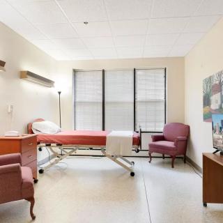 A clean and well-lit hospital room with a single bed and chairs.