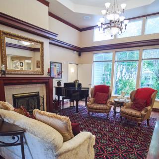 A cozy living room with elegant decor, featuring a grand piano, fireplace, and large windows.