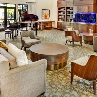 A spacious and elegant living room featuring comfortable seating, a grand piano, bookshelves, and an aquarium.
