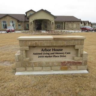 A sign in front of a care facility reads 'Arbor House Assisted Living and Memory Care' with the address.