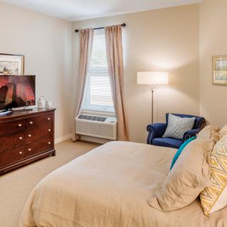 Cozy bedroom with a bed, dresser, and seating area.