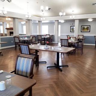 A spacious dining area with neatly arranged tables and chairs, featuring wood flooring and elegant lighting.