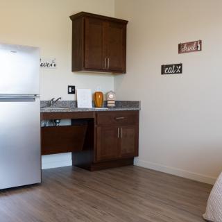 A simple kitchen area with a fridge, cabinets, and a sink on wooden flooring.