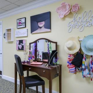 A stylish vanity area with a decorated wall featuring hats, artwork, and a mirror.