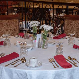 A formal dining table set with white linens, red napkins, flowers, and neatly arranged glassware.
