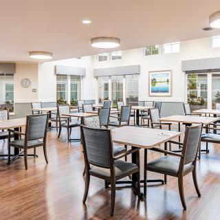A modern dining area with neatly arranged tables and chairs, featuring large windows and wooden flooring.