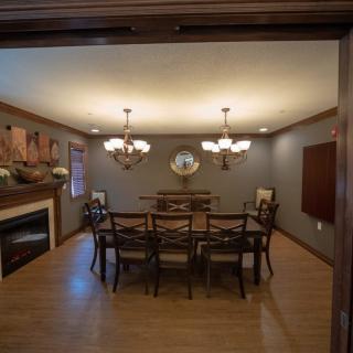 A cozy dining room with a large table, surrounded by chairs, and lit by elegant chandeliers.
