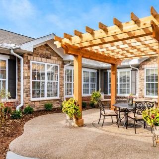 A cozy patio area with a wooden pergola and outdoor furniture, surrounded by well-maintained landscaping.