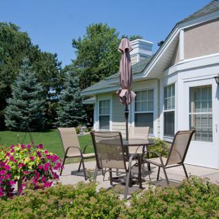 A serene backyard patio with outdoor furniture, surrounded by blooming flowers and a well-kept lawn.