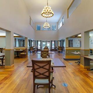 A spacious dining area with wooden floors, elegant chandeliers, and ample natural light.