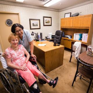 A caregiver smiles alongside an elderly patient in a welcoming office setting.