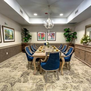 Elegant dining room with a large table and blue chairs under a chandelier.