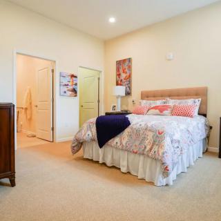A cozy bedroom with decorative bedding, artwork on the walls, and soft carpet flooring.