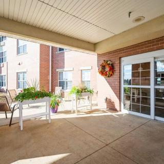 A welcoming porch area with chairs, tables, and potted plants at the entrance of a building.