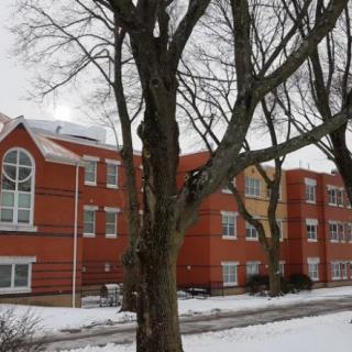 A red brick building surrounded by trees in a snowy winter setting.