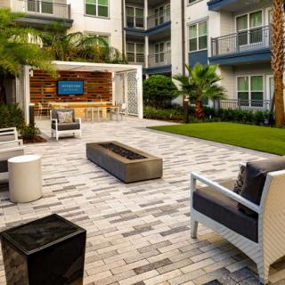 A modern outdoor patio area with comfortable seating and a television, set against the backdrop of an apartment complex.
