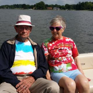 An elderly couple enjoying a boat ride on a sunny day, wearing colorful tie-dye shirts.