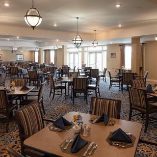 An elegant dining room with neatly arranged tables and chairs, featuring warm lighting.
