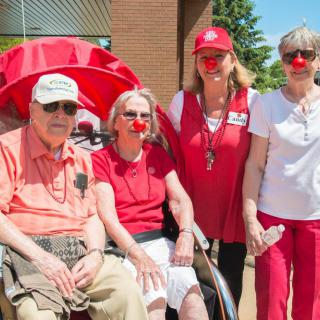 A group of people, some wearing red noses and red clothing, pose together outdoors, possibly during a charity event.