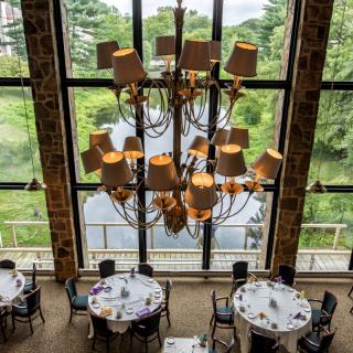 A beautifully set banquet hall showcasing a grand chandelier with large windows offering a view of lush greenery.