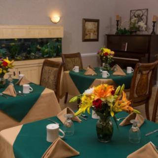 A cozy dining room with elegantly set tables and a piano in the background.