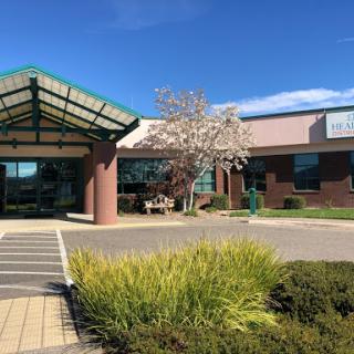 A healthcare facility with a welcoming entrance and blooming tree, set against a clear blue sky.