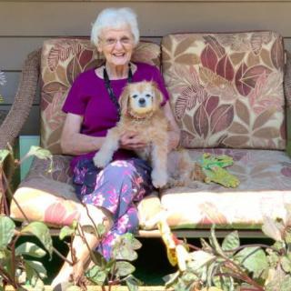 An elderly woman sitting on a garden bench holding her dog.