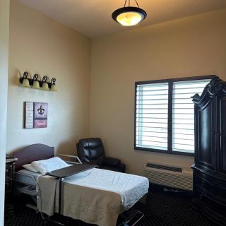 A hospital room with a single bed, recliner chair, and wooden cabinet.