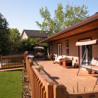 A cozy backyard patio with wooden decking and outdoor furniture, surrounded by a garden and fence.