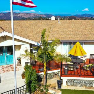 A backyard view featuring a patio with outdoor furniture, an American flag, and mountains in the background on a sunny day.
