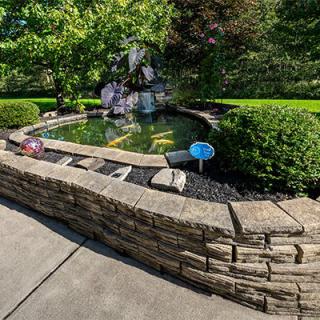 A serene garden pond enclosed by a stone wall and lush greenery.