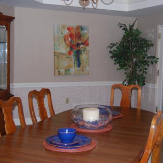 A cozy dining room with a wooden table, chairs, decorative artwork, and a plant in the corner.