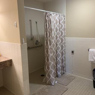 An accessible bathroom with a shower area featuring handrails, a patterned shower curtain, and a towel hanging on the wall.