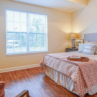 A cozy, well-lit bedroom with a neatly made bed and wooden flooring.