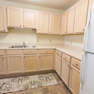 A clean and compact kitchen with light wood cabinets, a white refrigerator, and patterned flooring.