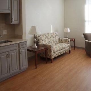 A cozy living room with a floral sofa and wooden flooring adjacent to a small kitchenette.