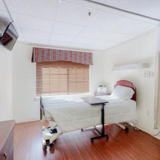 A well-lit and clean hospital patient room with a bed, television, and window.