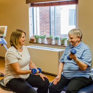 A healthcare professional guides an elderly individual in a weightlifting exercise, promoting strength and wellness.
