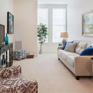 A cozy living room with modern decor, featuring a beige couch, television, and large windows.