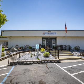 A building entrance with a flag and a small landscaped area in front of a parking lot.
