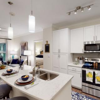 A modern kitchen with white cabinets and an island counter, featuring integrated appliances in an open layout.