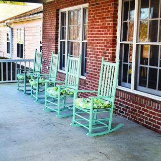 Four mint-green rocking chairs line a brick porch, inviting relaxation.