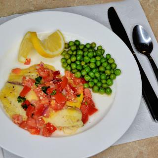 A healthy meal featuring fish with tomatoes and herbs, served with peas and lemon wedges.